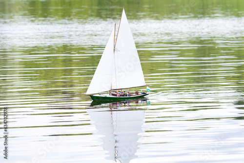 Remote control sail boat navigating in a calm lake. It has toys people to give sense of reality.