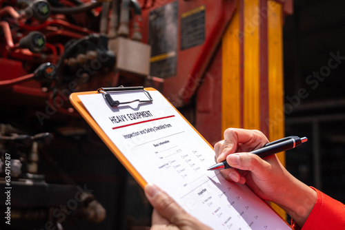 A mechanical engineer is inspecting the condition of truck crane vehicle (as blurred background) before start the operation on the inspection checklist form. Industrial working with safety practice. photo