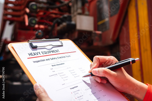 A mechanical engineer is inspecting the condition of truck crane vehicle (as blurred background) before start the operation on the inspection checklist form. Industrial working with safety practice.