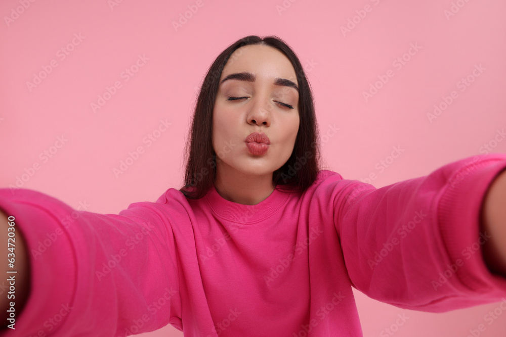 Young woman taking selfie and blowing kiss on pink background Young woman taking selfie and blowing kiss on pink background