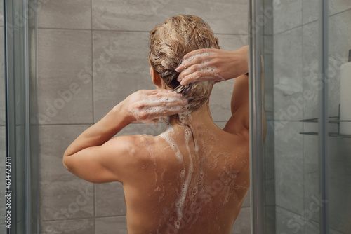 Woman washing hair in shower stall, back view