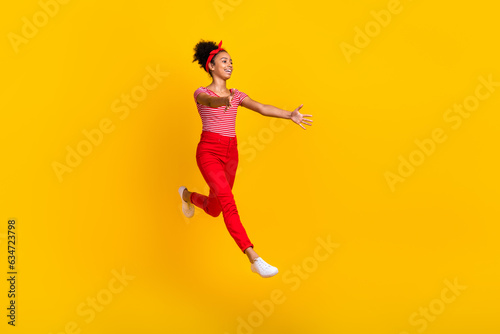 Full body profile photo of excited small beautiful girl jumping rush arms catch empty space isolated on yellow color background