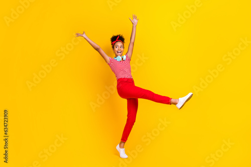 Full length photo of little carefree overjoyed girl dancing look empty space hang neck headphones isolated on yellow color background