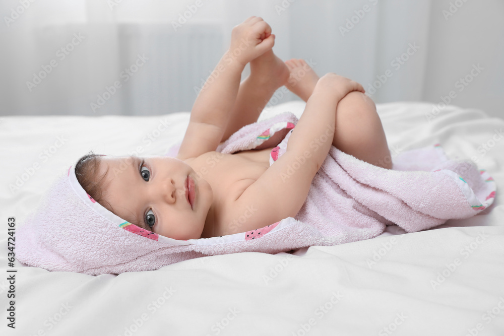 Naklejka premium Cute little baby in hooded towel after bathing on bed at home