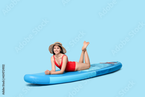 Happy woman resting on SUP board against light blue background