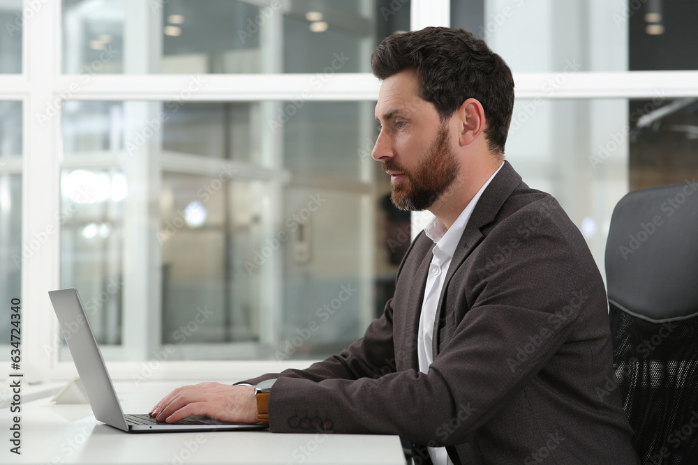 Man working on laptop at white desk in office Man working on laptop at white desk in office