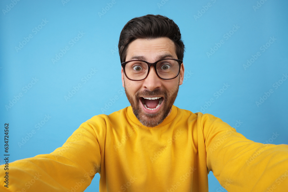 Happy man taking selfie on light blue background