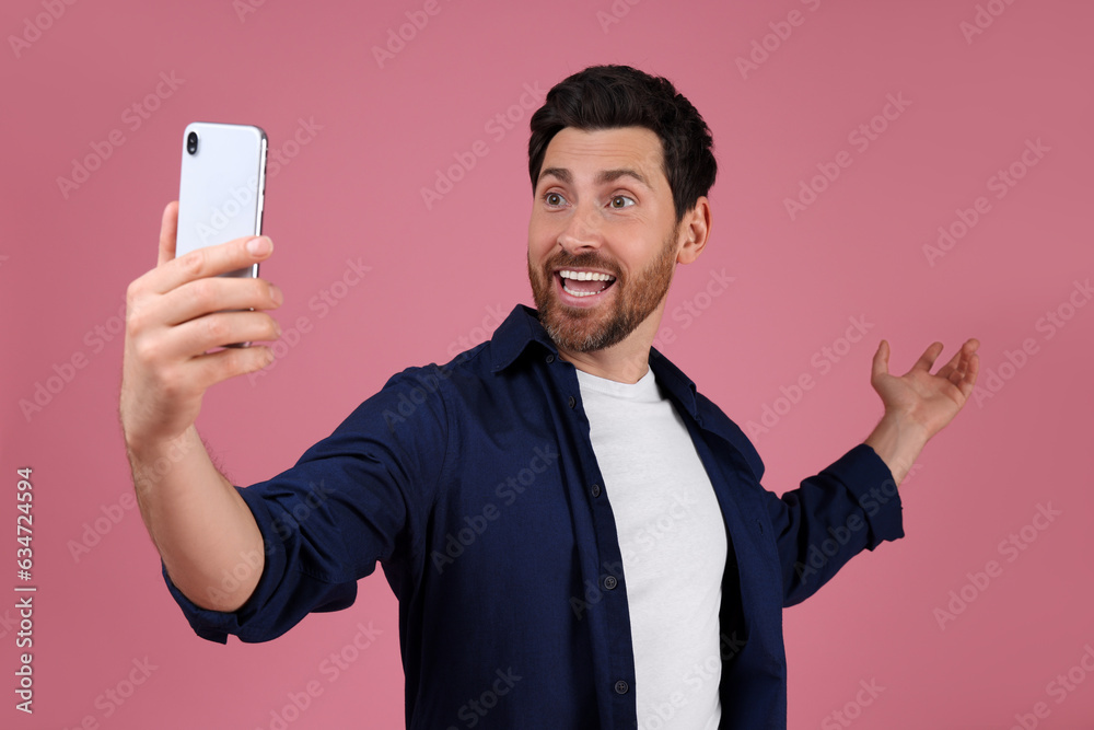 Smiling man taking selfie with smartphone on pink background Smiling man taking selfie with smartphone on pink background