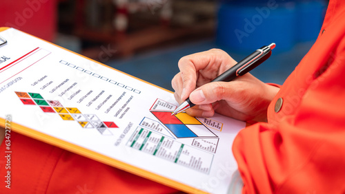 A safety engineer is using pen to rating the health risk assessment level of chemical hazardous material in the paperwork form. Industrial safety working scene, close-up and selecitve focus.