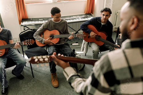 Male teenage students leaning guitar in music class at high school