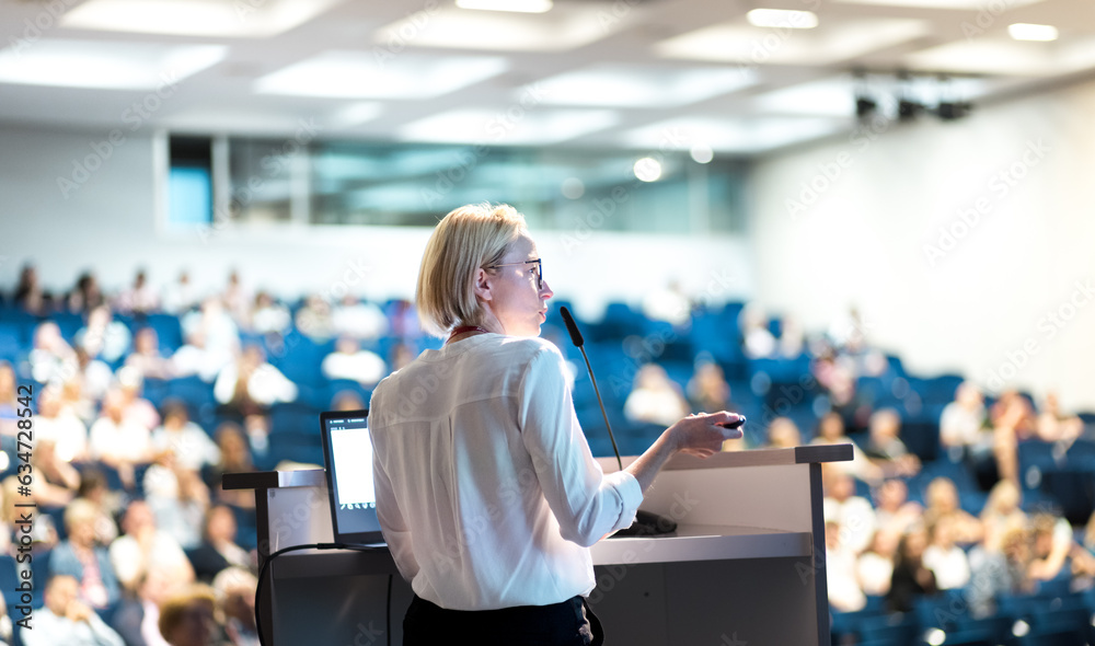 Female speaker giving a talk on corporate business conference. Unrecognizable people in audience at conference hall. Business and Entrepreneurship event Female speaker giving a talk on corporate business conference. Unrecognizable people in audience at conference hall. Business and Entrepreneurship event