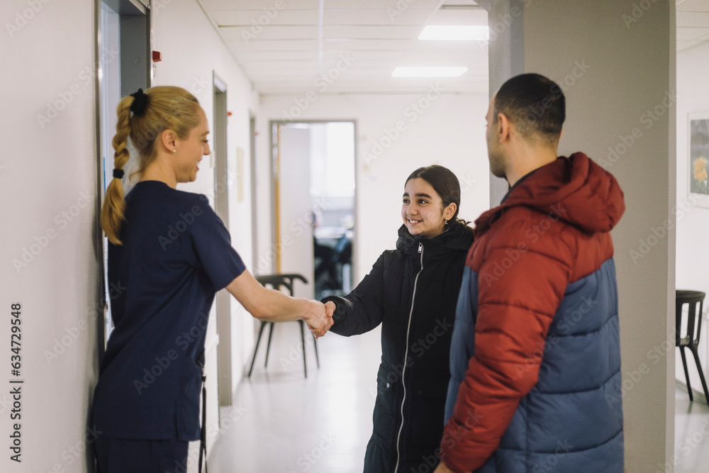 Smiling girl doing handshake with nurse standing in hospital corridor Smiling girl doing handshake with nurse standing in hospital corridor