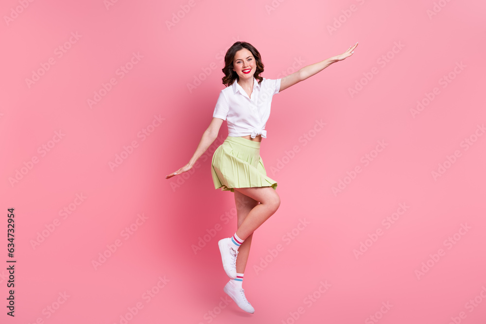 Full length photo of sweet carefree girl dressed white top jumping high arms sides isolated pink color background Full length photo of sweet carefree girl dressed white top jumping high arms sides isolated pink color background