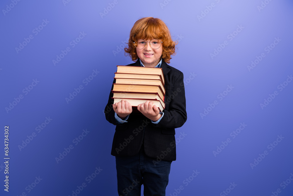 Portrait of cheerful smart schoolchild toothy smile hands hold pile stack book isolated on purple color background Portrait of cheerful smart schoolchild toothy smile hands hold pile stack book isolated on purple color background