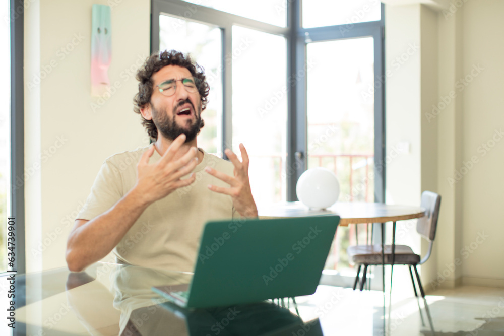 young adult bearded man with a laptop looking desperate and frustrated, stressed, unhappy and annoyed, shouting and screaming young adult bearded man with a laptop looking desperate and frustrated, stressed, unhappy and annoyed, shouting and screaming