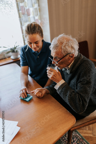 High angle view of senior man taking medicines while sitting with female caregiver at home