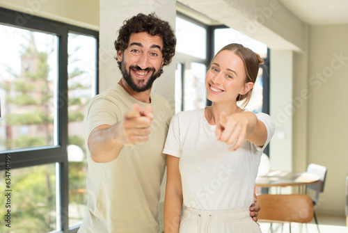 young adult couple pointing at camera with a satisfied, confident, friendly smile, choosing you