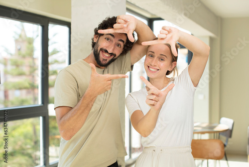 young adult couple feeling happy, friendly and positive, smiling and making a portrait or photo frame with hands