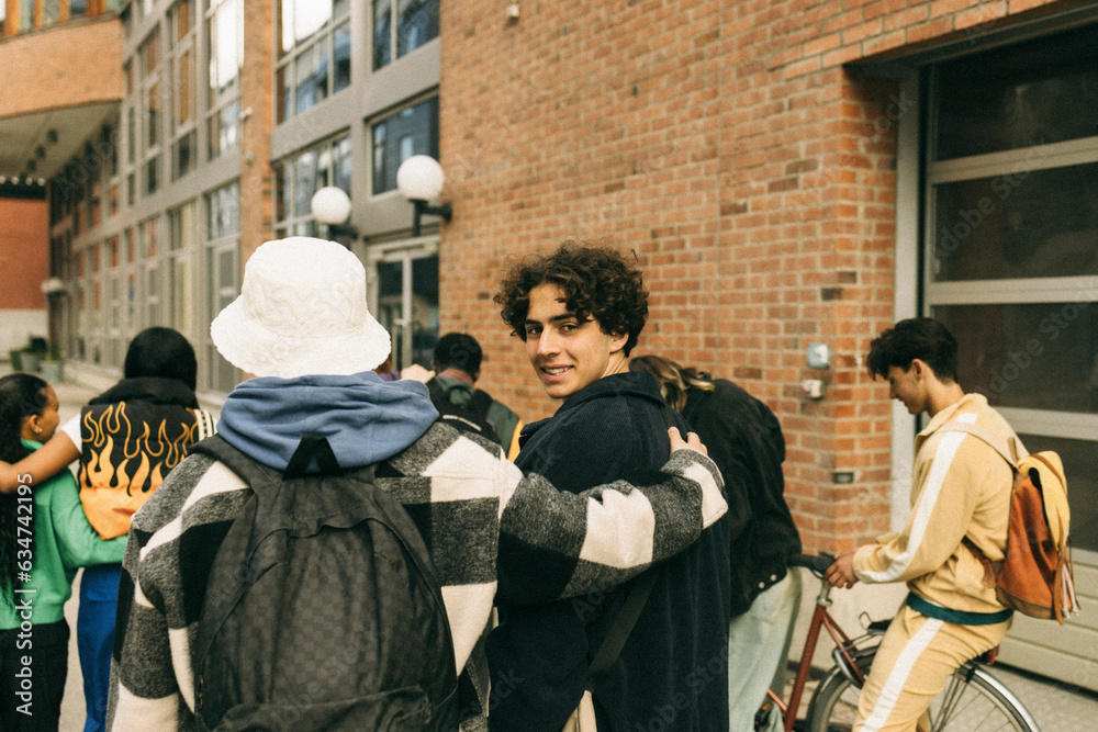Smiling teenage boy looking over shoulder while walking with friends on sidewalk Smiling teenage boy looking over shoulder while walking with friends on sidewalk