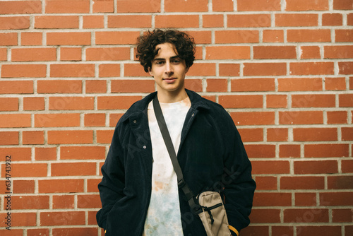 Portrait of teenage boy wearing jacket while standing against brick wall photo