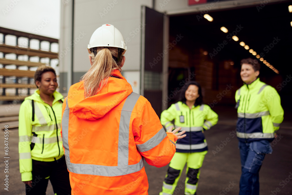 Rear view of female engineer in protective workwear discussing with workers at factory Rear view of female engineer in protective workwear discussing with workers at factory