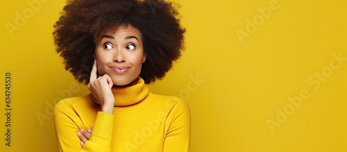 Excited African American woman with afro yellow studio background holds copy space on palm covering cheek