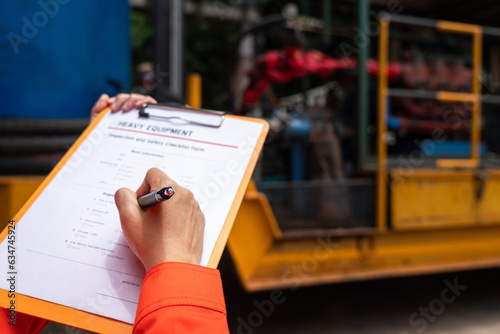 A mechanical engineer is checking on heavy machine and equipment inspection checklist form with the water pumping unit as background . Heavy industrial working action scene, selective focus.