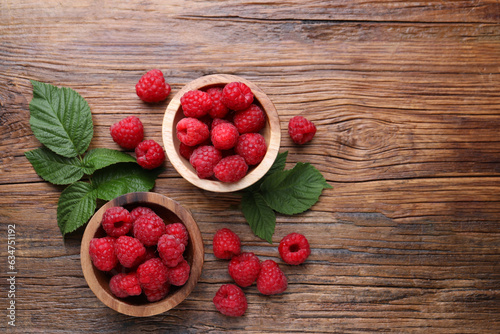 Tasty ripe raspberries and green leaves on wooden table, flat lay. Space for text