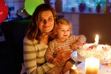 Adorable little toddler girl celebrating second birthday. Baby child daughter and young mother blowing candles on cake and candles. Happy healthy family portrait, mom love and happiness