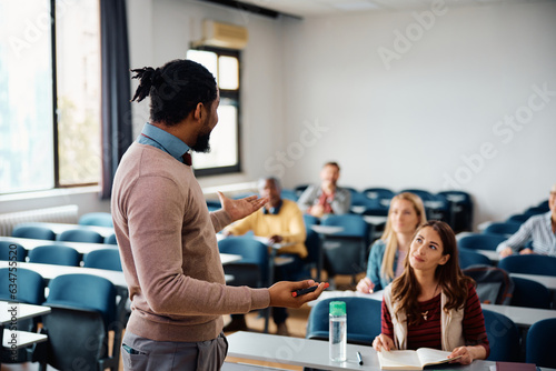 Black adult education teacher talks to group of students during lecture in classroom.