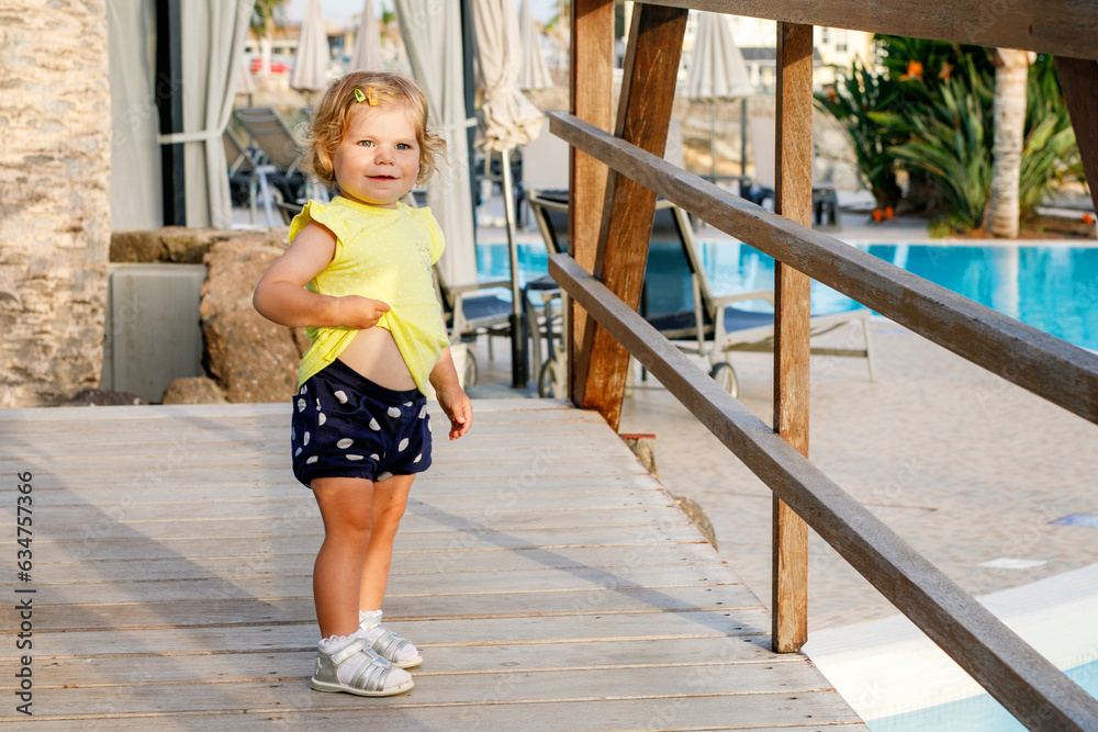 Happy blond little toddler girl having fun outdoor on vacations in family hotel with pool. Portrait of cute baby child