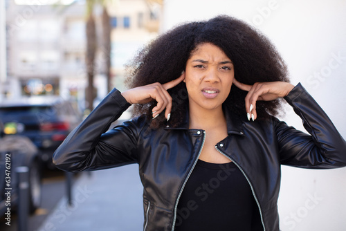 african american pretty woman looking angry, stressed and annoyed, covering both ears to a deafening noise, sound or loud music