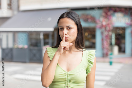 pretty hispanic woman looking serious and cross with finger pressed to lips demanding silence or quiet  keeping a secret