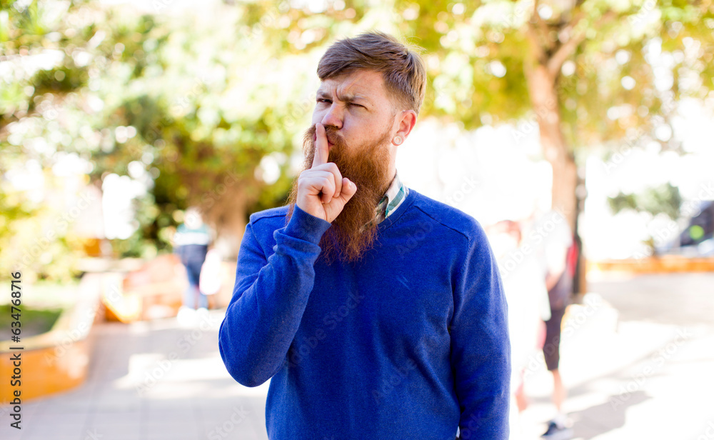 red hair bearded man looking serious and cross with finger pressed to lips demanding silence or quiet, keeping a secret red hair bearded man looking serious and cross with finger pressed to lips demanding silence or quiet, keeping a secret
