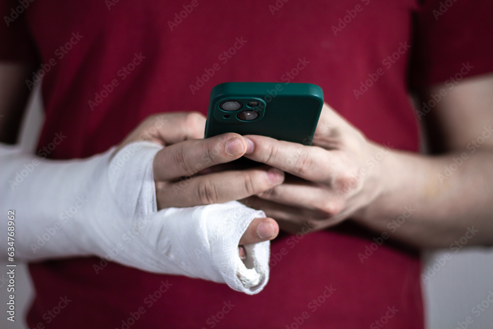 A man in a red T-shirt with a broken arm in a cast holds and uses a phone Close-up A man in a red T-shirt with a broken arm in a cast holds and uses a phone Close-up
