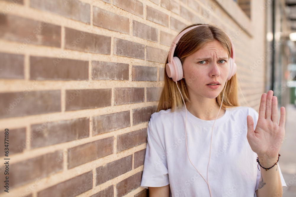 young pretty woman looking serious showing open palm making stop gesture. headphones and music concept young pretty woman looking serious showing open palm making stop gesture. headphones and music concept