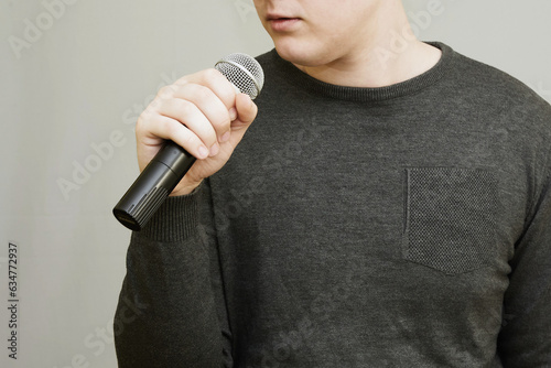 Young man holding a microphone in his hand in front of his face, which cannot be seen in its entirety. Public speaking, speaking genre photo