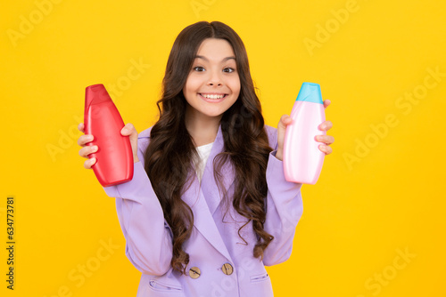 Teen child girl with shampoo bottle or shower gel isolated on yellow background. Kids hair cosmetic product. Happy teenager, positive and smiling emotions of teen girl. photo