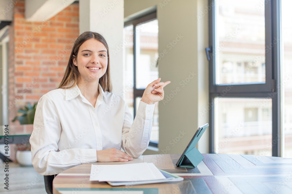 young pretty woman smiling cheerfully, feeling happy and pointing to the side. telecommuting concept young pretty woman smiling cheerfully, feeling happy and pointing to the side. telecommuting concept