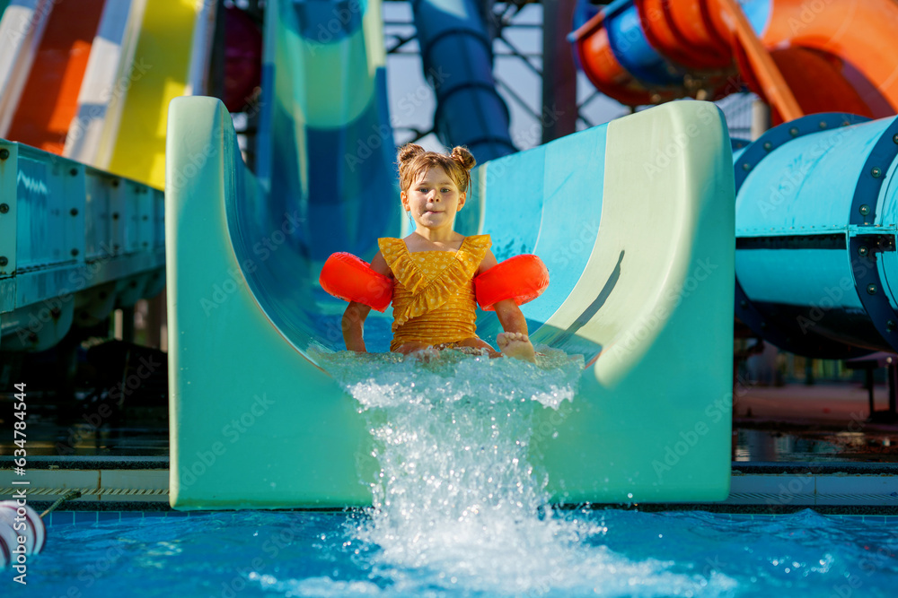 Little preschool girl on water slide in aqua park. Happy child having ...