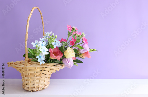 image of delicate pink flowers in the wicker basket over wooden table and purple background