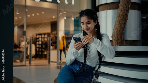 Female student middle-eastern girl businesswoman arabian ethnic woman student shopper chatting on phone sit at shopping center use mobile apps purchasing online read digital news watch internet video