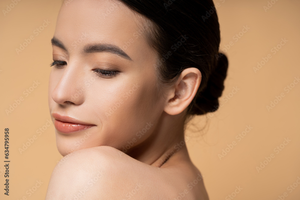 Young asian woman with naked shoulder and natural makeup posing while standing isolated on beige