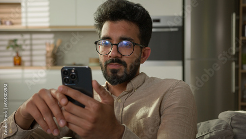 Photos Arabian Indian ethnic man guy use mobile phone on couch browsing mobile internet