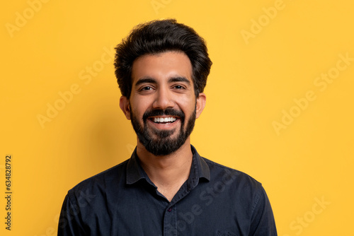 Portrait of handsome smiling indian man posing on yellow studio background © Prostock-studio