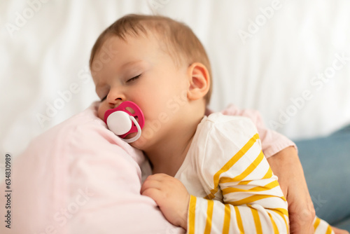 Vászonkép Adorable infant girl on mother's hands sucking pacifier and sleeping peacefully,