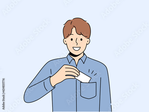 Man takes out business card from pocket to exchange contacts with potential partner or buyer and looks into camera with smile. Business guy in blue shirt wants to share contacts with new acquaintances