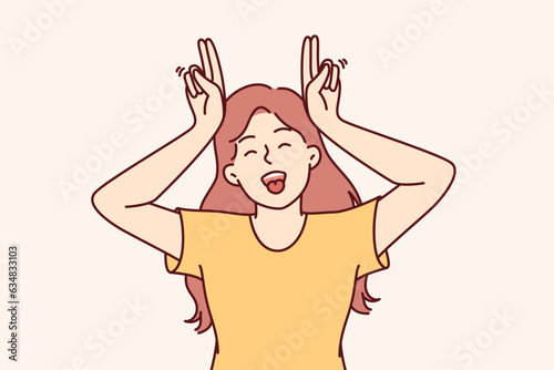 Little funny girl makes horns from fingers and shows tongue, wanting to cheer up others and friends. Teenage girl laugh making comical grimace and fool around refusing to become adult