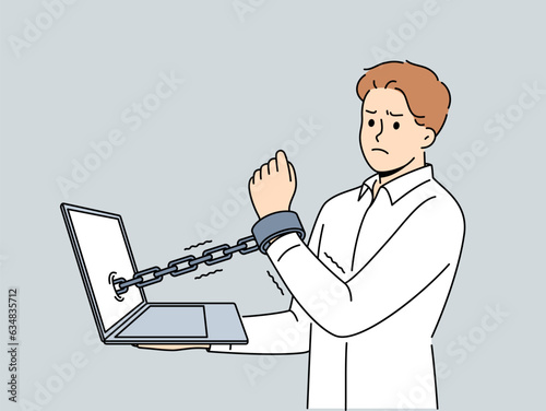 Man handcuffed to laptop symbolizes slavery of clerks and freelancers working through internet. Guy suffers from online addiction and slavery or lack of time for rest associated with strict deadlines