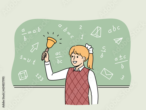 Girl elementary school student with bell stands near chalkboard with mathematical formulas and examples. Happy schoolgirl with bow on blond hair makes call, for concept back to school